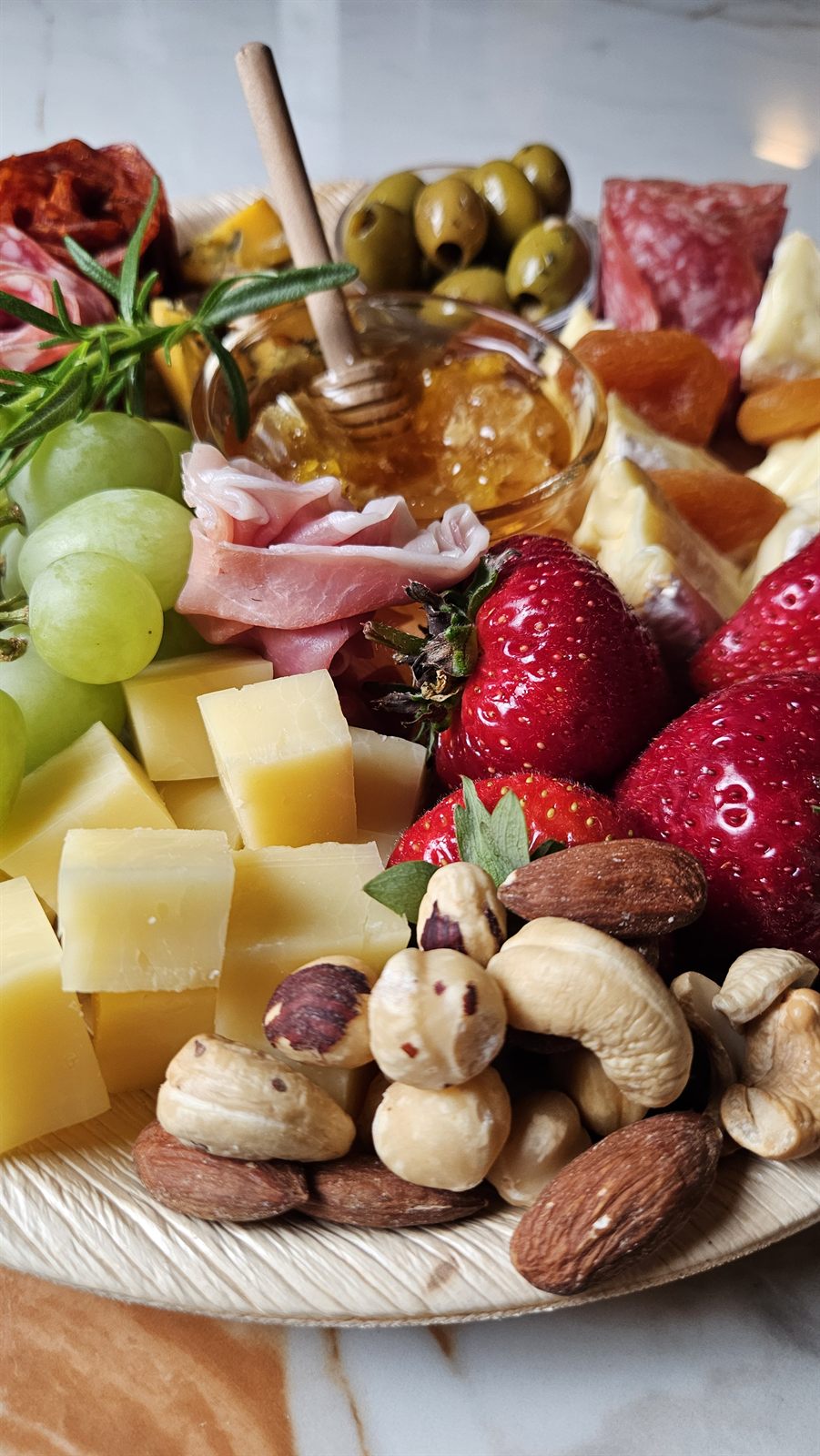 The edge of a board with cheeses, mixed nuts, strawberries, olives and honey