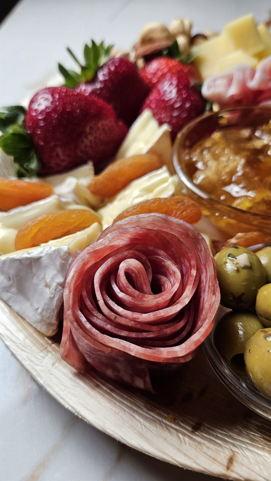 A hand-folded salami rose with brie, apricots and strawberries