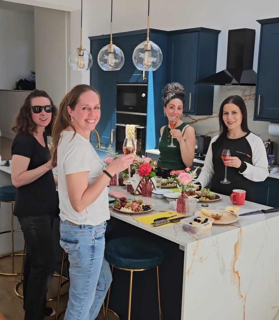 Four friends with drinks, flowers and grazing boards at a Social Nibble workshop in a home kitchen
